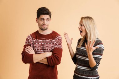 Portre tahriş olmuş bir genç çiftin birlikte ayakta kazak giymiş tartışıyor bej renkli arka plan üzerinde izole