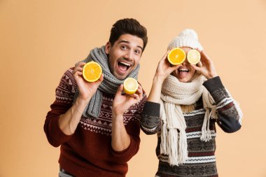 Kazak ve birlikte ayakta eşarp genç gülümseyen bir çift portresi dilimlenmiş limon ve portakal gösterilen bej renkli arka plan üzerinde izole