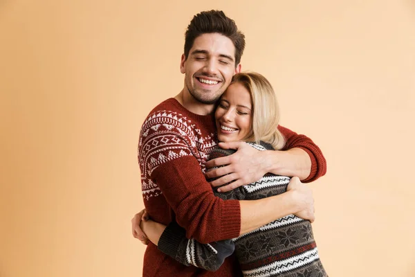 ベージュの背景の上分離したハグのセーターでカップルを愛して幸せな若者のイメージ — ストック写真
