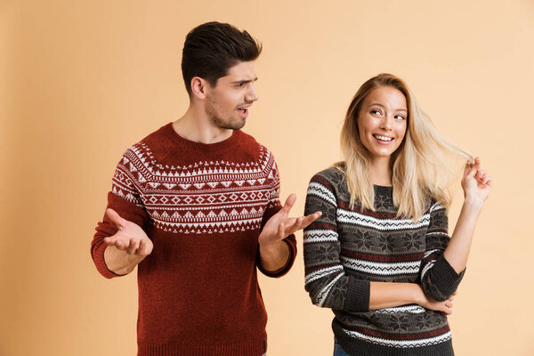 Image of displeased young man looking at flirty woman who looking aside playing with hair.