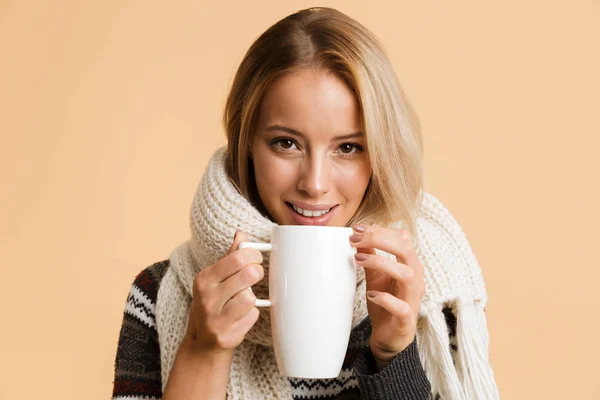 セーターを着た幸せな女の子と熱いお茶のカップを保持しているベージュの背景の上分離したスカーフの肖像画間近します — ストック写真