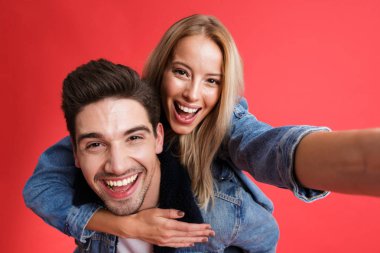 Mutlu bir genç çift birlikte ayakta kot ceketler içinde giyinmiş portresi alarak bir selfie, Atçılık, kırmızı arka plan üzerinde izole