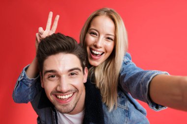 Birlikte ayakta kot ceketler içinde giyinmiş genç gülümseyen bir çift portre çekici bir selfie, Atçılık, kırmızı arka plan üzerinde izole