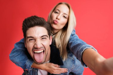 Komik bir genç çiftin birlikte ayakta kot ceketler içinde giyinmiş portre çekici bir selfie, Atçılık, kırmızı arka plan üzerinde izole