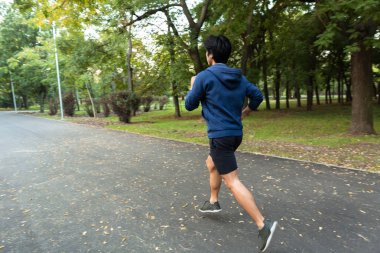 Kulaklık ile müzik dinlemek parkta, koşu bir Asyalı gencin arkadan görünüm