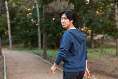 Görüntü gülümseyen Asya'ya ait adam rahat kıyafet ve park yeşil ağaçlar ile yolda yürürken gözlük