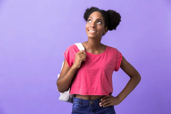 バックパックの笑みを浮かべて 紫色の背景に分離された上方を見て身に着けている率直なアフリカ系アメリカ人の女性学生の写真 — ストック写真