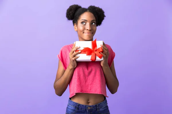 幸せのアフリカ系アメリカ人女性と紫色の背景に分離した赤の弓でプレゼント ボックスを押し笑顔の写真 — ストック写真
