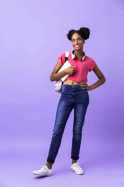 紫色の背景に分離した練習帳を保持のバックパックを身に着けているアフリカ系アメリカ人の女性学生の完全な長さの写真 — ストック写真