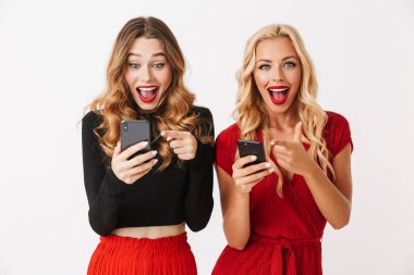 Cep telefonları, kutlama kullanarak makyaj ayakta beyaz arka plan üzerinde izole giyen iki heyecanlı genç akıllıca giyimli kadın portresi