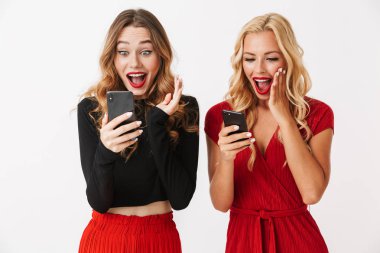 Cep telefonları, kutlama kullanarak makyaj ayakta beyaz arka plan üzerinde izole giyen iki heyecanlı genç akıllıca giyimli kadın portresi