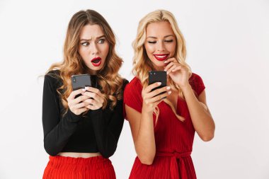 Cep telefonları birbirine bakarak beyaz arka plan üzerinde iki heyecanlı genç akıllıca giyimli kadın makyaj ayakta giyen portresi izole
