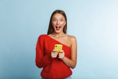 Cep telefonu kullaranarak mavi duvar arka plan üzerinde izole görüntü poz güzel duygusal heyecanlı genç bir kadın.