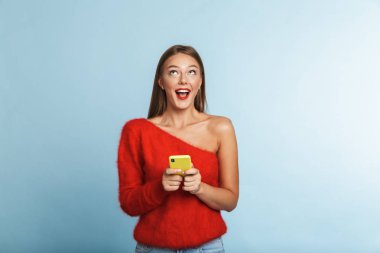 Cep telefonu kullaranarak mavi duvar arka plan üzerinde izole görüntü poz güzel duygusal heyecanlı genç bir kadın.