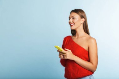 Cep telefonu kullaranarak mavi duvar arka plan üzerinde izole görüntü güzel bir gülümseyen genç kadının poz.
