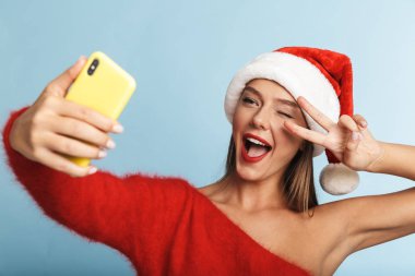 Mavi duvar arka plan üzerinde izole poz güzel duygusal heyecanlı genç kadın giyen Noel şapka görüntüsünü almak bir selfie cep telefonuyla.