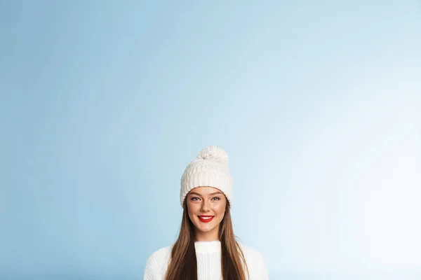 一个美丽的可爱的年轻女子的形象穿着冬天的帽子摆在蓝色墙壁背景被隔绝 — 图库照片