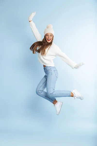 一个美丽的可爱的年轻女子的形象穿着冬天帽子跳跃查出蓝色墙壁背景 — 图库照片