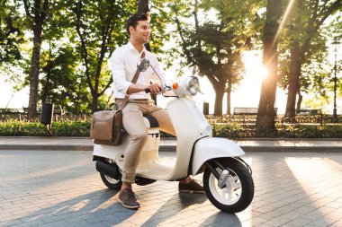 Açık havada scooter üzerinde yürüyen bir yakışıklı genç iş adamı görüntüsü.