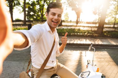 Açık havada scooter üzerinde yürüyen bir yakışıklı heyecanlı genç iş adamı fotoğrafını çekin bir selfie kamera tarafından.