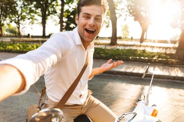 Açık havada scooter üzerinde yürüyen bir yakışıklı heyecanlı genç iş adamı fotoğrafını çekin bir selfie kamera tarafından.
