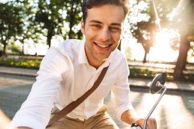 Açık havada scooter üzerinde yürüyen bir yakışıklı heyecanlı genç iş adamı fotoğrafını çekin bir selfie kamera tarafından.