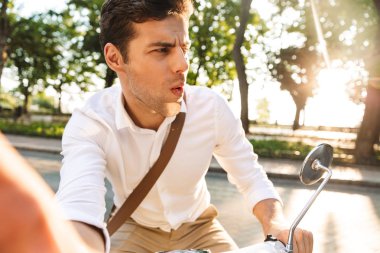 Açık havada scooter üzerinde yürüyen bir yakışıklı şok genç iş adamı fotoğrafını çekin kamera bir kenara bakarak bir selfie.