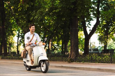 Açık havada scooter üzerinde yürüyen bir yakışıklı genç iş adamı görüntüsü.