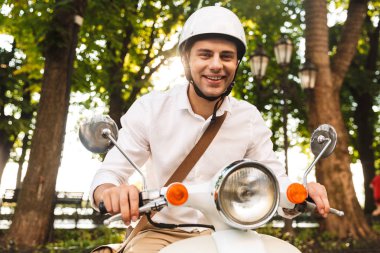 Şehir Parkı'nda açık havada bir motosiklet sürme kask içinde heyecanlı genç işadamı