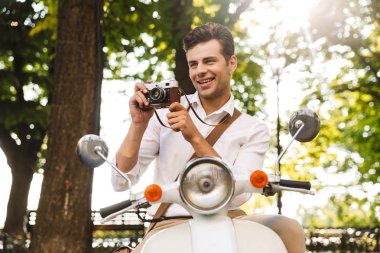 Mutlu genç işadamı açık havada, bir motosiklet üzerinde bir fotoğraf makinesi ile fotoğraf çekimi sürme