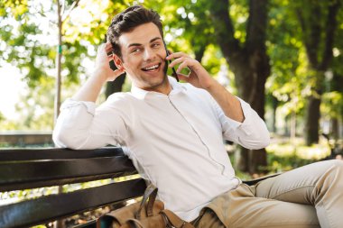 Cep telefonu üzerinde konuşurken açık havada, bankta oturan mutlu genç işadamı