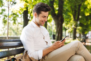 Genç işadamı açık havada, banktaoturuyor cep telefonu arıyorum gülümseyen