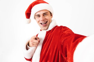 Neşeli adam 30'lu Noel Baba kostüm ve kırmızı şapkalı Studio beyaz arka plan üzerinde izole selfie fotoğraf çekerken gülüyor portresi