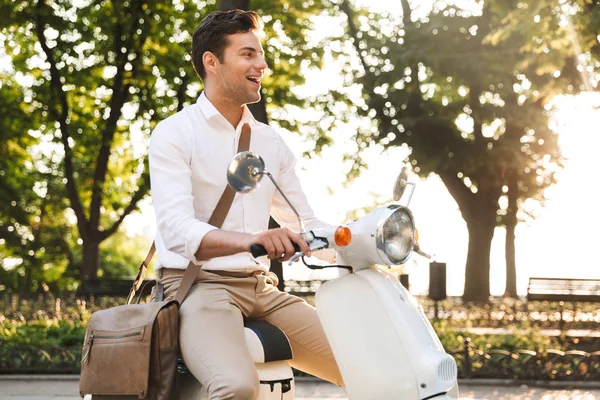 Image of a handsome young business man walking outdoors on scooter.