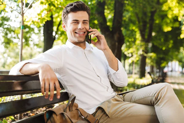 Szczęśliwy Młody Biznesmen Siedząc Ławce Zewnątrz Rozmowy Telefon Komórkowy — Zdjęcie stockowe