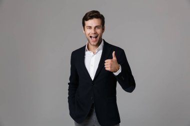 Yakışıklı işadamı 30s mutlu gülümseme gri arka plan üzerinde izole kamera başparmak gösteren resmi kıyafetli görüntüsünü
