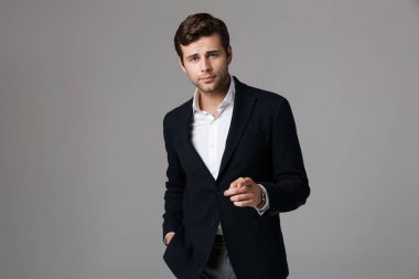 Parmak kamera işaret gri arka plan üzerinde izole takım elbise giymiş bir yakışıklı genç işadamı portresi kapatın