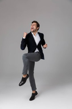 Tam boy görüntü iyimser işadamı 30'lu bağırıyor ve gri arka plan üzerinde izole yumruk kenetlenmesi resmi elbiseli