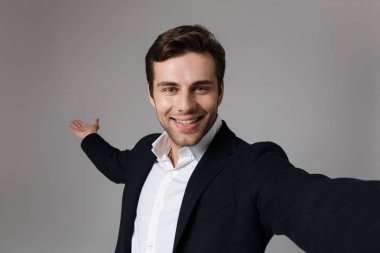 Görüntü gri arka plan üzerinde izole selfie fotoğraf çekerken kameraya gülümseyen resmi kıyafetli iyimser işadamı 30'lu