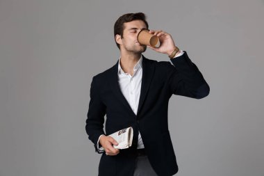 Görüntü çekici adamın 30'lu kahve içme ve gri arka plan üzerinde izole gazete tutan takım elbise