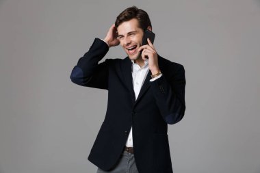 Görüntü olumlu adamın 30'lu takım elbise gri arka plan üzerinde izole siyah Smartphone cep telefonu ile konuşma