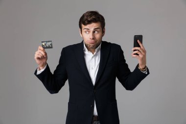 Beyaz adam 30'lu holding siyah cep telefonu ve kredi kartı gri arka plan üzerinde izole iş elbiseli görüntüsünü