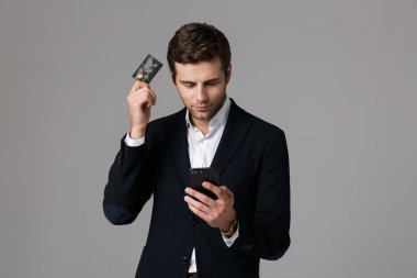 Görüntü kredi kartı ve cep telefonu gri arka plan üzerinde izole kullanarak takım elbiseli emin işadamı 30'lu