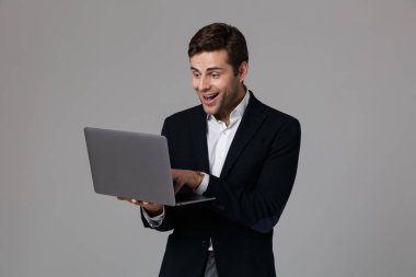 Çok mutlu bir genç işadamı portresi dizüstü bilgisayar kullanan, gri arka plan üzerinde izole takım elbise giymiş