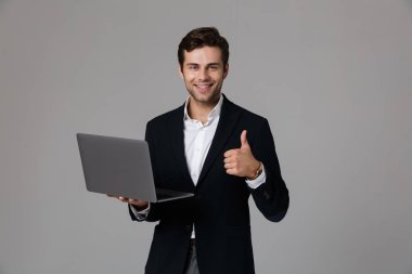 Görüntü gri arka plan üzerinde izole laptop kullanırken sevindirici takım elbiseli neşeli işadamı 30'lu