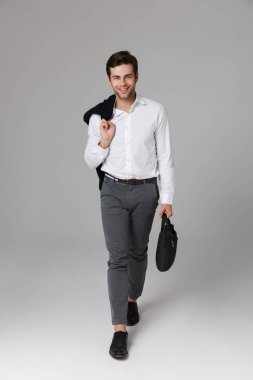 Tam boy görüntü ciddi adam elinde çanta ile yürüyüş ve ceket gri arka plan üzerinde izole omzunun üzerinden tutan 30s