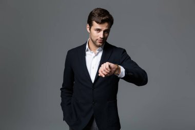 Kendine güvenen genç işadamı portresi onun kol saati görünümlü gri arka plan üzerinde izole takım elbise giymiş