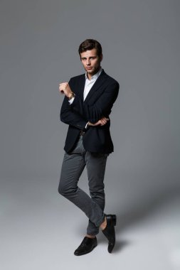 Yakışıklı bir genç işadamı portresi tam uzunlukta kameraya bakarak poz, gri arka plan üzerinde izole takım elbise giymiş