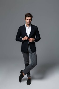 Ciddi bir genç işadamı portresi tam uzunlukta kadar ceketinin düğmelerini poz, gri arka plan üzerinde izole takım elbise giymiş