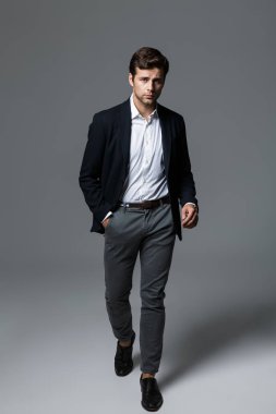 Yakışıklı bir genç işadamı portresi tam uzunlukta yürüyüş kameraya bakarak poz, gri arka plan üzerinde izole takım elbise giymiş